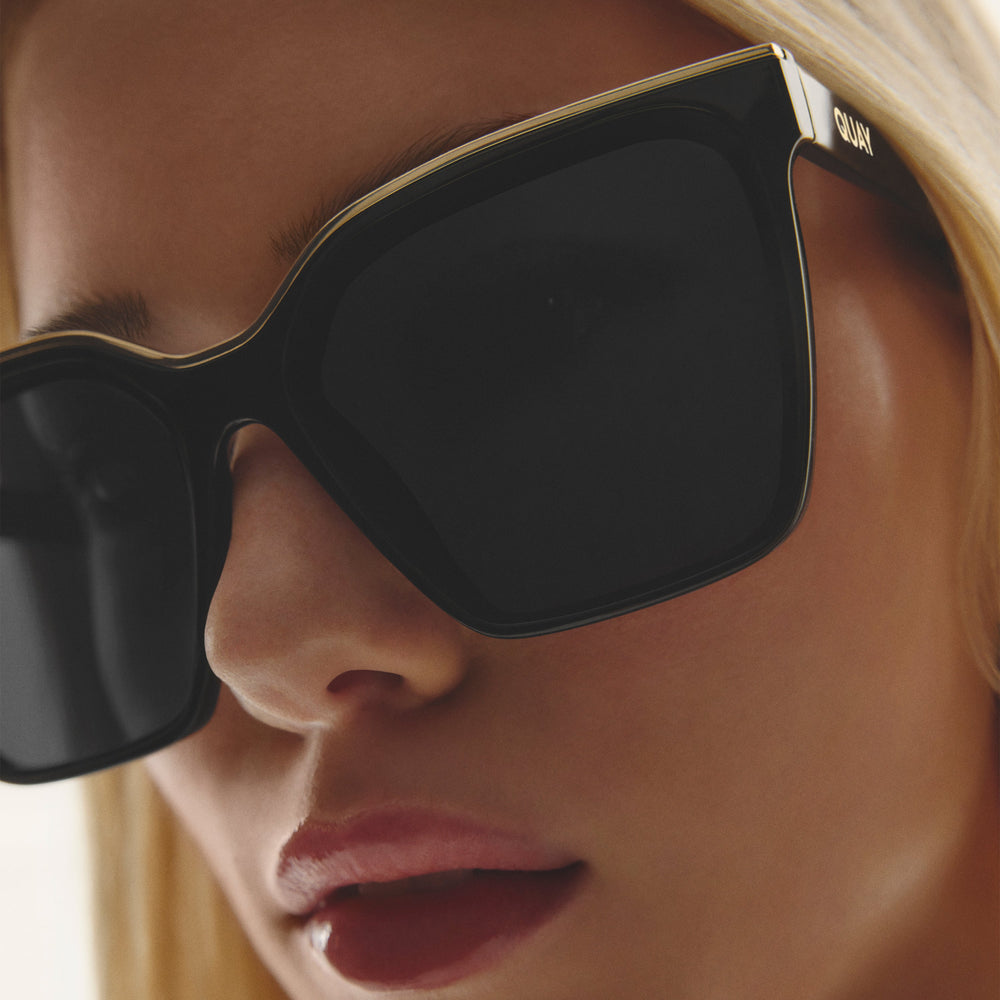 Detail shot of model wearing QUAY LEVEL UP black square brow bar sunglasses with gold details